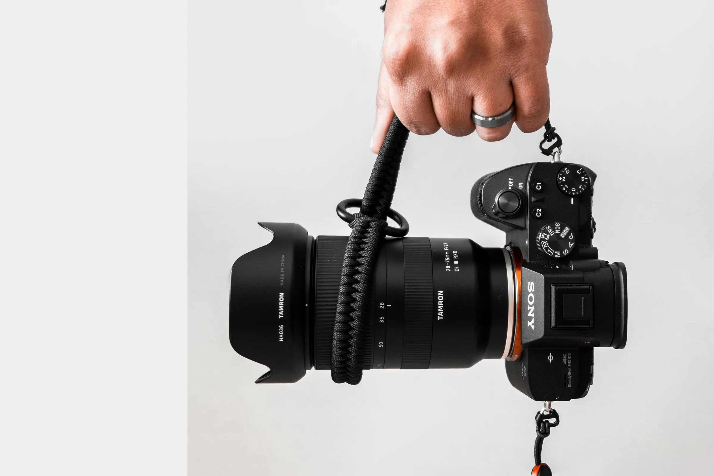 A hand holding a Sony mirrorless body with a Tamron 28-75mm zoom, hanging from a wrist strap.